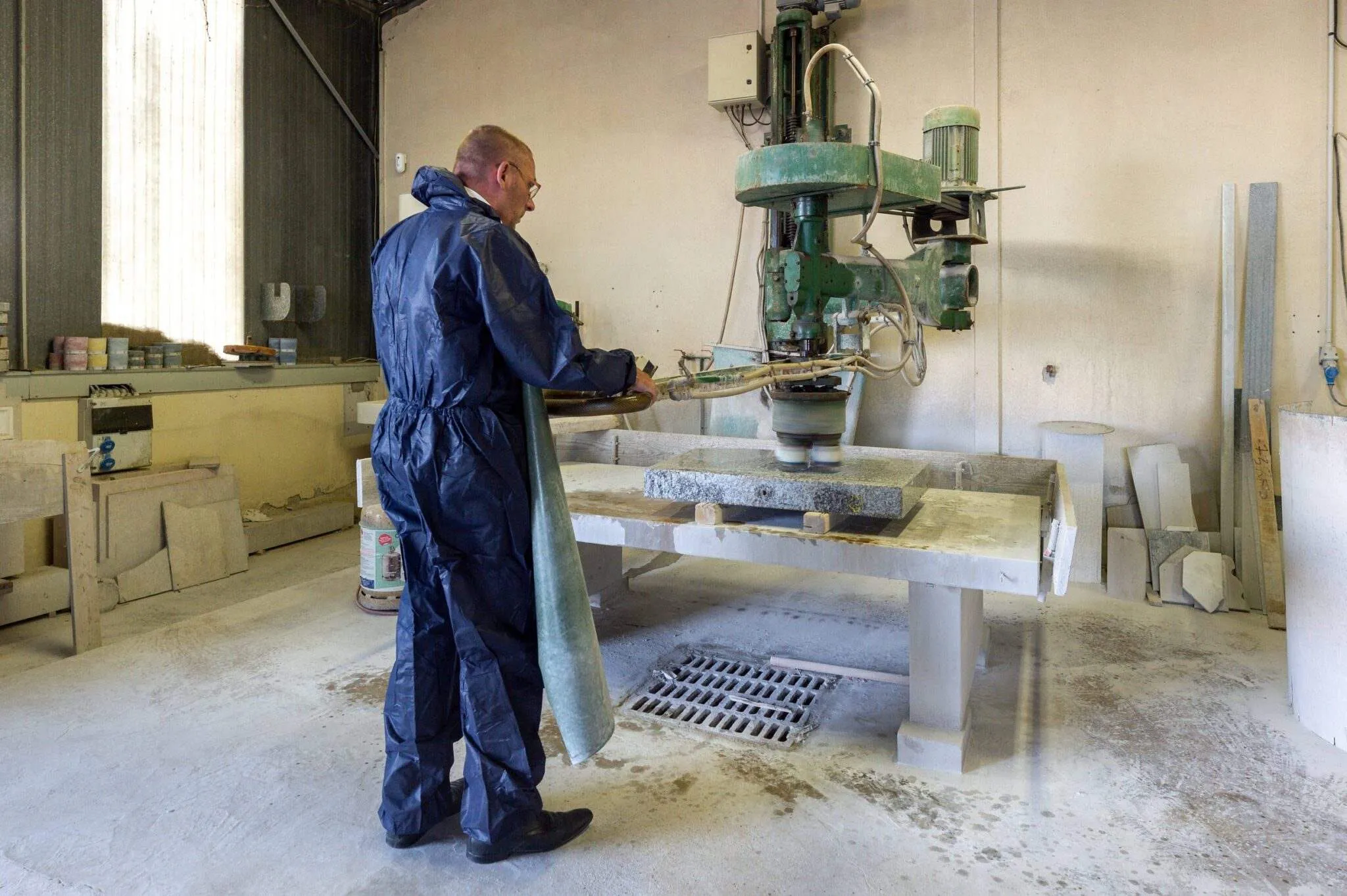 Artisan marbrier en combinaison de protection polissant une plaque de granit en atelier