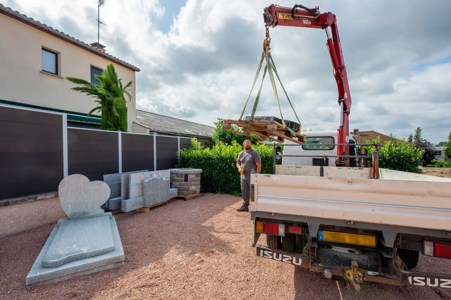 Marbrier funéraire déchargeant une stèle en pierre à l'aide d'un camion-grue sur un chantier